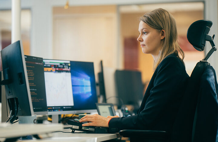 Kuvituskuva, jossa nainen tekee töitä tietokonenäyttöjen ääressä.
