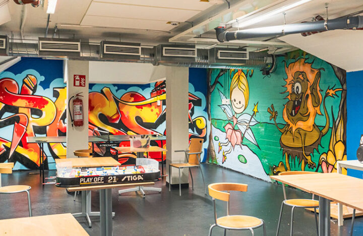 Värikkäin seinämaalauksin koristeltu tila, jossa pelejä ja pöytiä.
